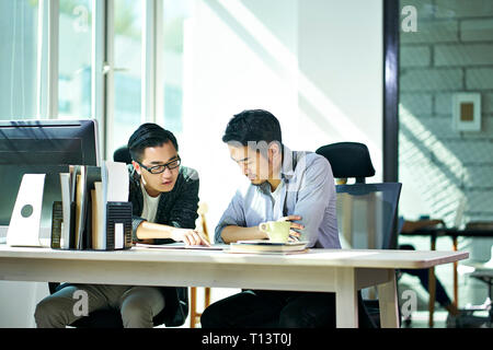 two young asian corporate executives working together discussing business plan in office.