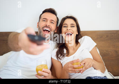 Happy couple watching TV in bed Stock Photo