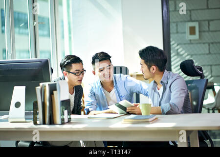 three young asian corporate executives working together discussing business plan in office. Stock Photo