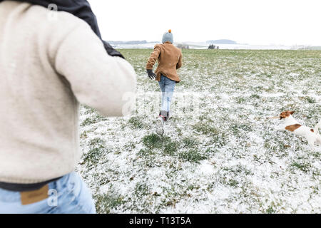 Father, son and dog running on snowy field in winter Stock Photo