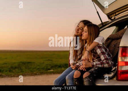 Two happy sisters sitting at opened tail watching sunset together Stock Photo