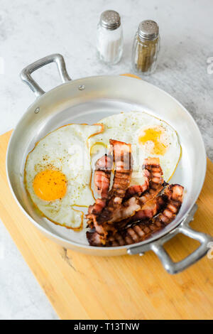 Fried eggs and bacon in pan Stock Photo