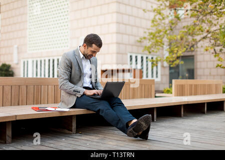 Smiling businessman sitting on a bench using laptop Stock Photo