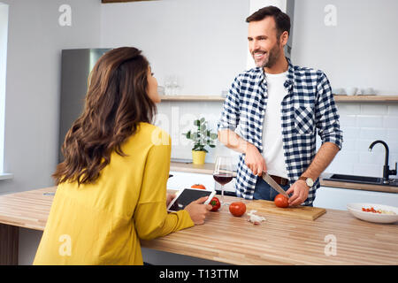 Affectionate couple in kitchen, preparing spaghetti toghether, using digital tablet Stock Photo