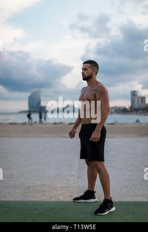 Barechested muscular man standing outdoors at dusk Stock Photo