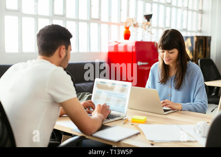 Colleagues using laptops at desk in office Stock Photo