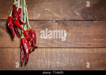 Red chili peppers hangs on a wooden wall to dry. Close-up view with space for text. Stock Photo