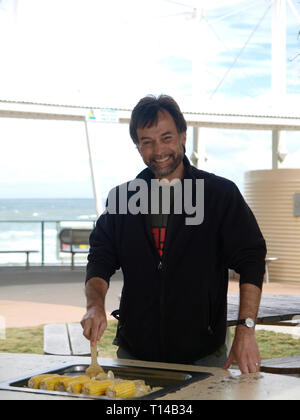 Smiling man cooking a barbecue on the Sunshine Coast, Queensland, Australia with the ocean in the background Stock Photo