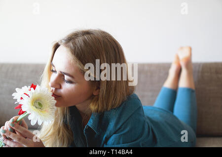 Attractive young woman sniffing bouquet of flowers lying on the couch