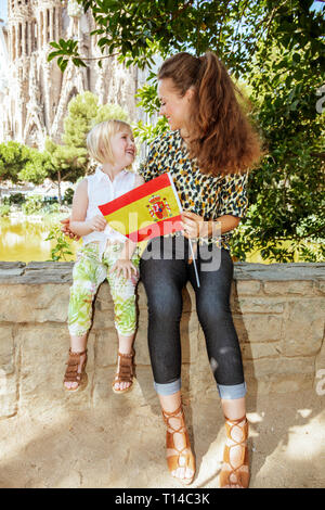 Barcelona - August, 06, 2015: smiling stylish mother and daughter tourists with Spanish flag looking at each other against La Sagrada Familia in Barce Stock Photo