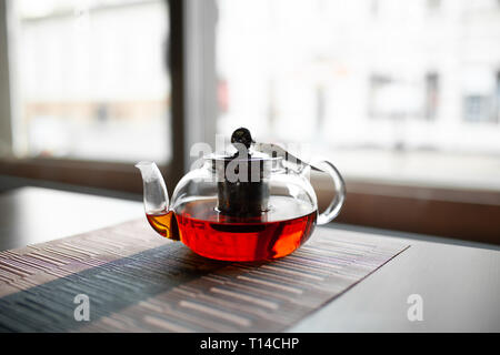 Glass transparent teapot of invigorating fresh aromatic tea on a wooden table Stock Photo