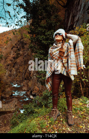 happy stylish woman hiker in poncho and sunglasses in the forest enjoying promenade. Stock Photo