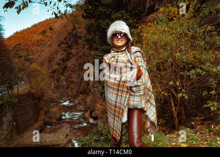 happy modern traveller woman in poncho and sunglasses outdoors enjoying promenade. Stock Photo