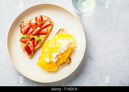 Vegan fruit sandwiches with mango, strawberry and peanut butter on a white plate. Stock Photo