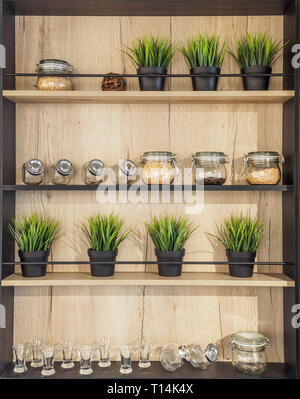 Wooden helf with kitchenware. Glass jars with spices pot plant glasses on the wooden rack kitchen background Stock Photo