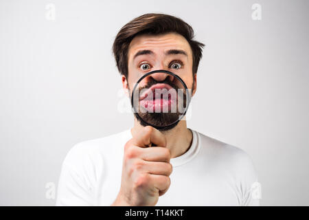 Strange and amazed man Isolated on white background and making some fun with putting a loupe in front of his mouth. Guy looks quite unusual from this  Stock Photo