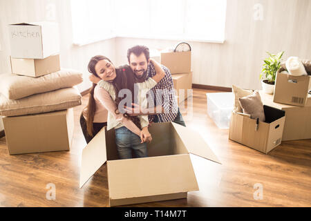 Cheerful young parents are hugging their daughter together. They have found her in a box. She hided there. Family has just moved to a new apartment an Stock Photo