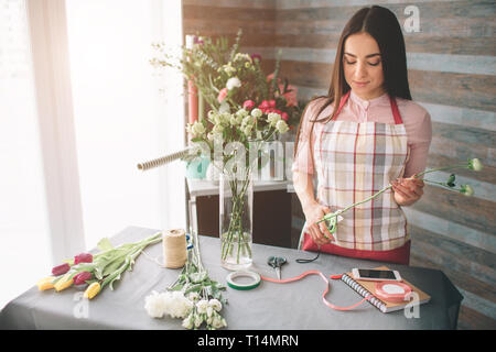 Female florist at work: pretty young dark-haired woman making fashion modern bouquet of different flowers. Women working with flowers in workshop Stock Photo