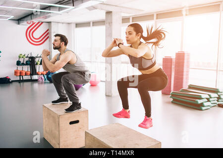 A picture of slim and well-built young man and woman doing jumps on platform. It is a hard exercise but they are doing it successful and with Stock Photo