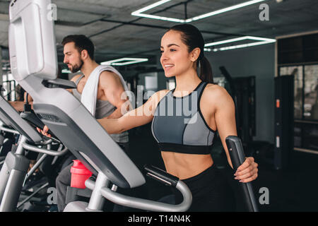 Two young sport folks are exercising on the elliptical machine. They are having a tough workout. Stock Photo