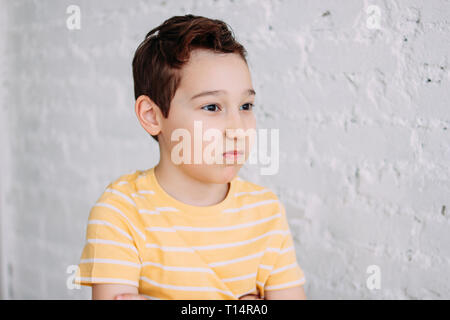 Cute tween angry boy with funny face in yellow t-shirt isolated on white brick wall background Stock Photo