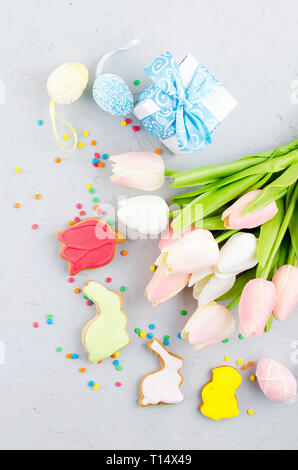 Easter colorful gingerbread cookies,  small decorative eggs in the nest and tulips on light grey concrete background, top view,  copy space, Easter gr Stock Photo