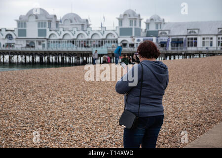 Middle aged woman using mobile phone at the beach with pier in the background Stock Photo