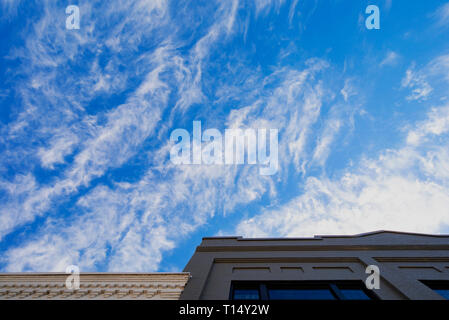 Cirrus clouds against a deep blue sky above old brick buidlings. Stock Photo