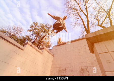 A young guy performs a jump through the space between the concrete parapets. The athlete practices parkour, training in street conditions. The concept Stock Photo