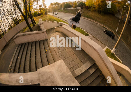 A young guy performs a side flip in the autumn park. The athlete practices parkour, training in street conditions. The concept of sports subcultures a Stock Photo