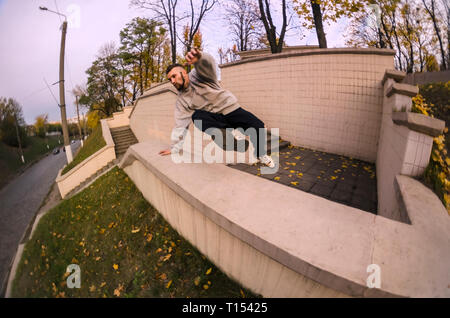 A young guy performs a jump through the concrete parapet. The athlete practices parkour, training in street conditions. The concept of sports subcultu Stock Photo