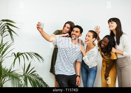Playful colleagues standing at brick wall taking a selfie Stock Photo