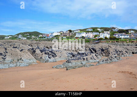 Craggy rocks on Woolacombe Beach with a view of hotels, seafront apartments, and other buildings, from Woolacombe Bay, Devon, UK Stock Photo