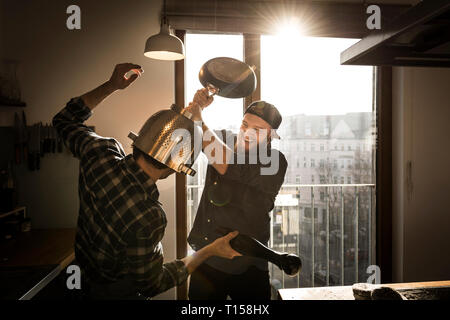 Friends having a duel with a colander and a pan in the kitchen Stock Photo