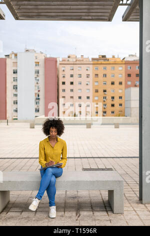 Woman sitting on bench taking notes Stock Photo