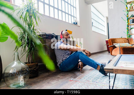 Young man with headphones sitting on floor in a loft Stock Photo