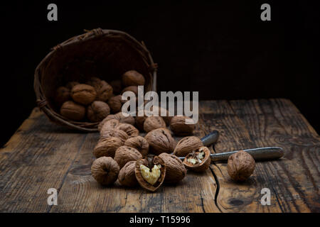 Whole and cracked walnuts, nutcracker and wickerbasket on wood Stock Photo