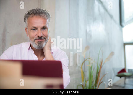 Portrait of confident businessman in a loft using laptop Stock Photo