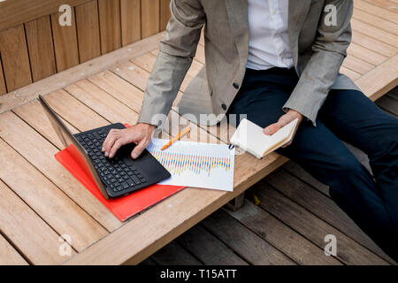 Close-up of businessman sitting on a bench using laptop and diary Stock Photo