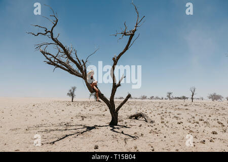 Namibia, Way to Sossusvlei, woman sitting in dead tree in the desert Stock Photo