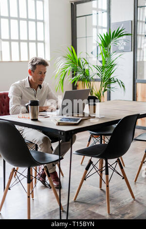Businessman using laptop at desk in a loft office Stock Photo