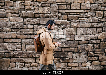 Spain, Igualada, man walking along stone wall using cell phone Stock Photo