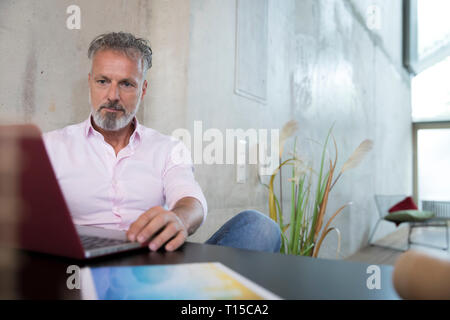 Businessman sitting at table in a loft using laptop Stock Photo