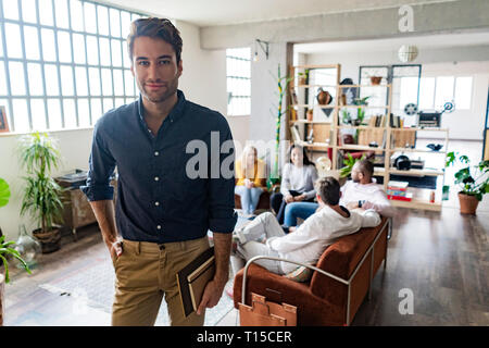Portrait of confident young businessman with coworkers in background in loft office Stock Photo