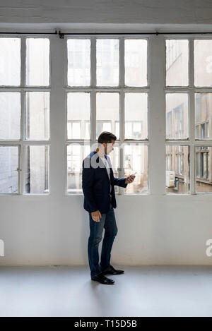 Businessman standing in a loft at the window using cell phone Stock Photo