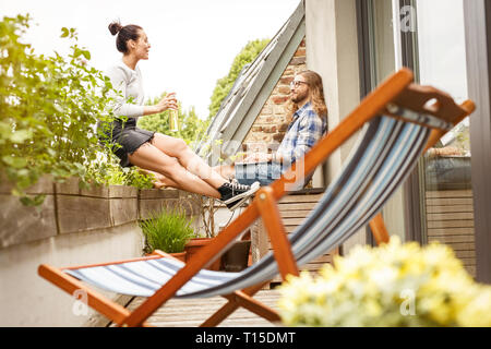 Young couple sitting on their balcony in summer, talking and using laptop Stock Photo