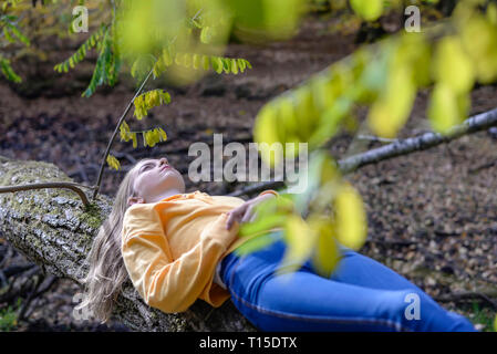 Girl lying on tree trunk in the autumnal forest relaxing Stock Photo