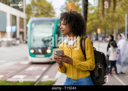 Woman with backpack and headphones using smartphone in the city Stock Photo