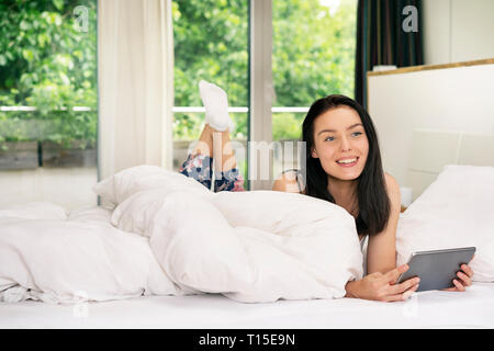 Young woman lying bed, using digital tablet in the morning Stock Photo