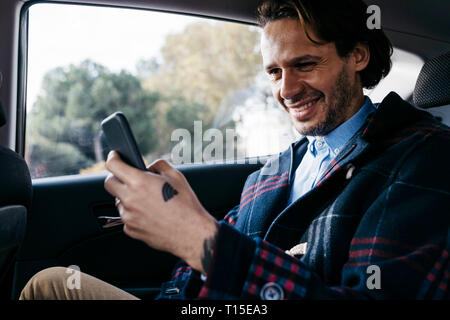 Smiling man sitting on back seat of a car using cell phone Stock Photo